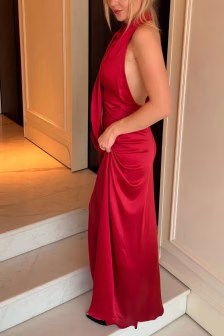 Woman in a red satin floor-length dress standing on a marble staircase, shown in side profile.