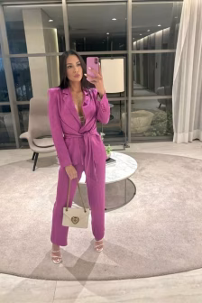 Woman in a magenta pantsuit posing in a mirror selfie, holding a pink phone and a beige handbag with a gold chain.