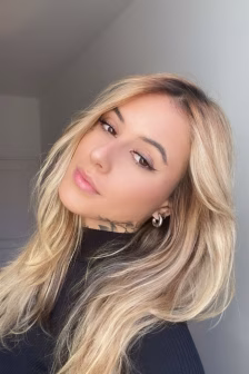 Close-up portrait of a woman with long blonde hair wearing a black top, looking softly at the camera with a neutral expression.
