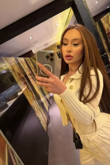 Woman with long brown hair takes a mirror selfie in a cream ribbed outfit in a stylish restroom.