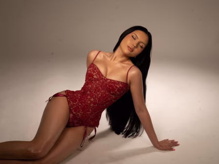Woman in red lace bodysuit lounging on a studio floor with eyes closed.