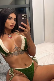 Self-portrait of a woman in a green bikini taking a mirror selfie with a smartphone; tattoos along her torso visible and a belly button piercing.