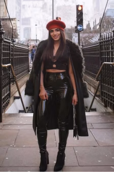 Woman in a red beret, black fur coat, and glossy black outfit posing on a city sidewalk.